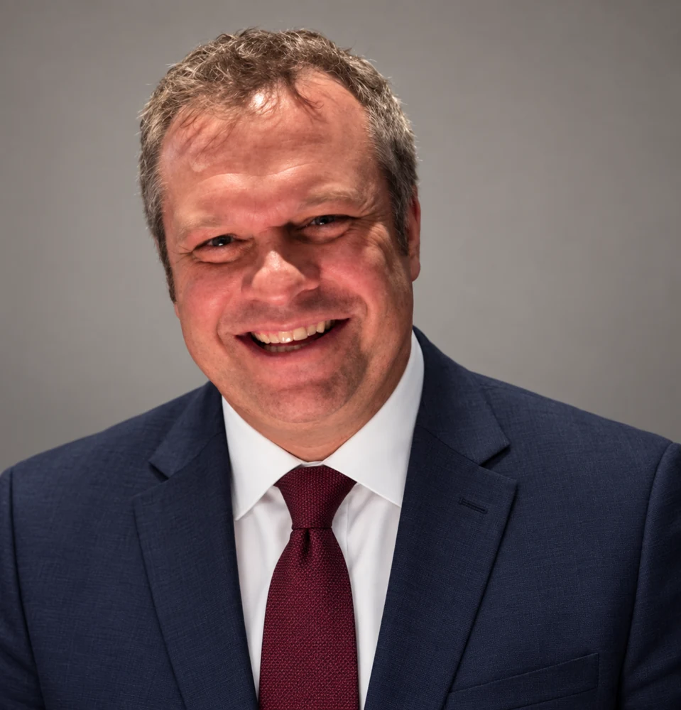 Peter Reynolds wearing a navy suit, white shirt, and burgundy tie